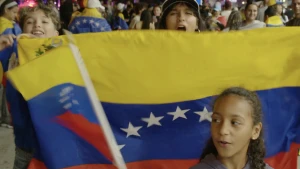 Een afbeelding met drie kinderen, zij juichen en hebben een Venezolaanse vlag vast.