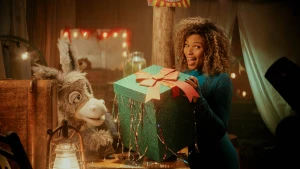 Een foto van de presentatrice en het ezeltje. De presentatrice heeft een groot groen cadeau met een strik in haar armen.