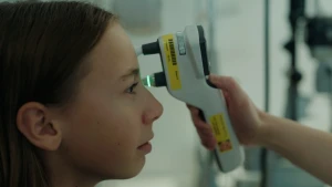 Foto van meisje en profil die haar ogen laat onderzoeken door een hand die een apparaat bij haar linkeroog houdt.