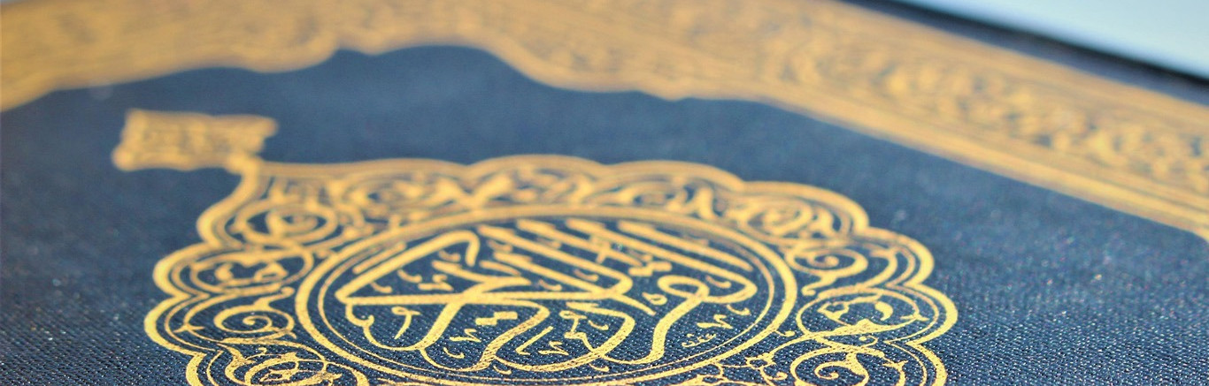 Foto van de omslag van een Koran, donkerblauw met gouden tekens.