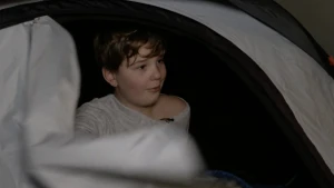 Een afbeelding van een jongen die net zijn tent heeft opengeritst. Het is nog donker buiten en de jongen draagt een pyjama.