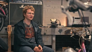 Een foto van een jongen die in een garage zit omringt door fietsen.