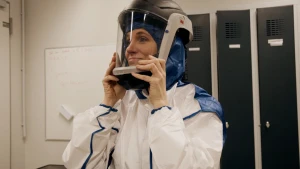 Foto van presentatrice Petra Grijzen die in een wit pak en helm met kijkvenster bij zichzelf opzet, in voorbereiding op een maanwandeling op aarde.