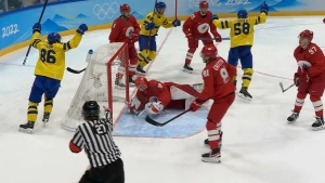 Foto van ijshockeywedstrijd waarbij het gele team net heeft gescoord in het doel van het rode team. De keeper ligt op het ijs en de spelers in het geel juichen.