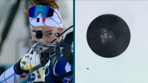 Foto van biatlonatlete die met geweer aan het mikken is op schietschijf, die zichtbaar is in het rechterdeel van de foto.