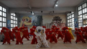 Foto van zaal in Chinese stijl waar kinderen oefenen voor de traditionele leeuwendans. Een stuk of twintig kinderen zijn verkleed in rode pakken en vooraan in het midden staat de witte leeuw met grote ogen.