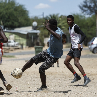 Voetballende jongeren op zand.