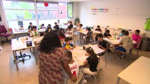 Foto van een klaslokaal die vol zit met kinderen. In de voorgrond zie je de rug van de juf.