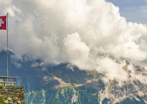 Zwitserse vlag met op de achtergrond bergen en wolken.
