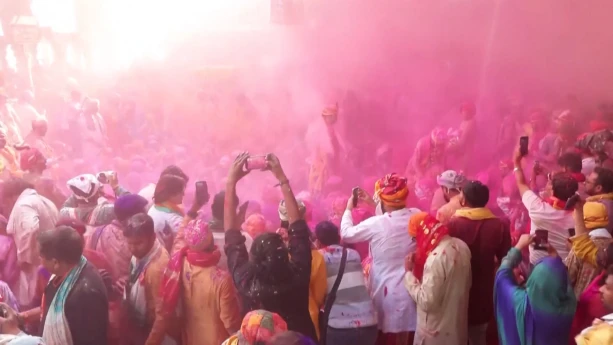 Foto van mensen op straat in India die Holi vieren; de lucht is gevuld met roze verfpoeders.