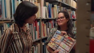 Een foto van twee vrouwen in een archief, de ene laat een kookboek aan de ander zien.