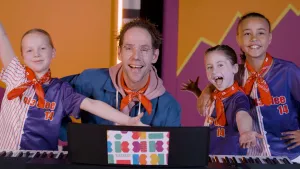 Foto van zangcoach Michiel met drie lachende meisjes van Kinderen voor Kinderen.